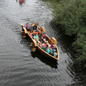 Eine Gruppe von Mädchen* und Frauen* sitzt in einem Tretboot auf einem Fluss.