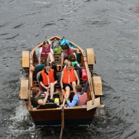 Eine Gruppe von Mädchen* und Frauen* sitzt in einem Tretboot auf einem Fluss.