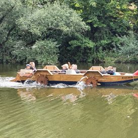 Eine Gruppe von Mädchen* und Frauen* sitzt in einem Tretboot auf einem Fluss.